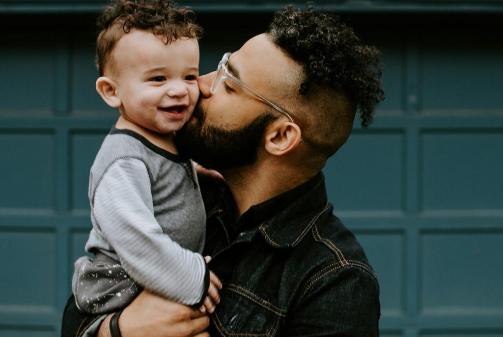 A man hugs his young son in front of their home.