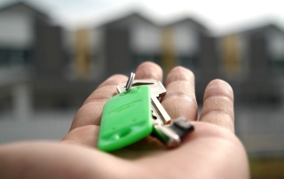 A hand holds keys in front of a house